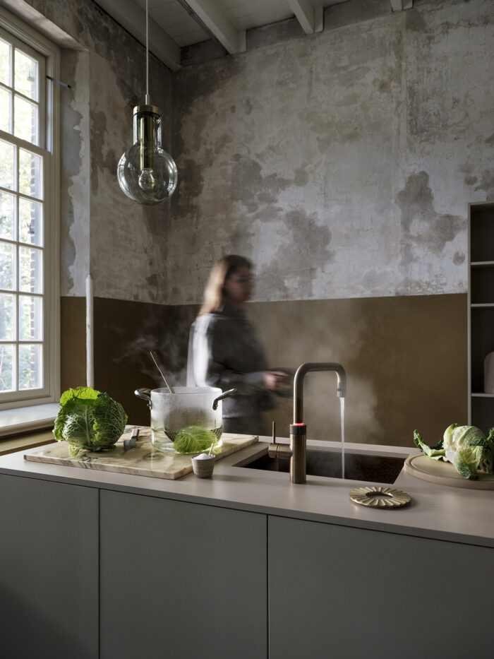 Quooker Armatur mit kochendem Wasser neben dampfendem Topf und Gemüse in moderner Küche