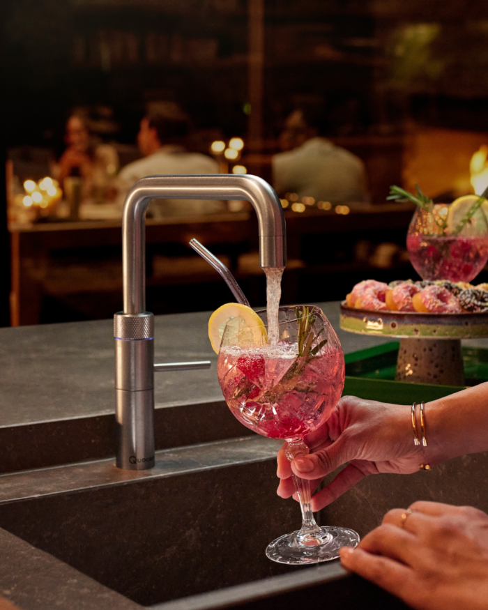 Quooker Wasserhahn füllt ein Cocktailglas mit Sprudelwasser in stilvoller Küchen- und Barumgebung