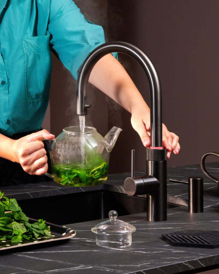 Schwarze Quooker Armatur füllt eine Glaskanne mit heißem Wasser für frischen Minztee